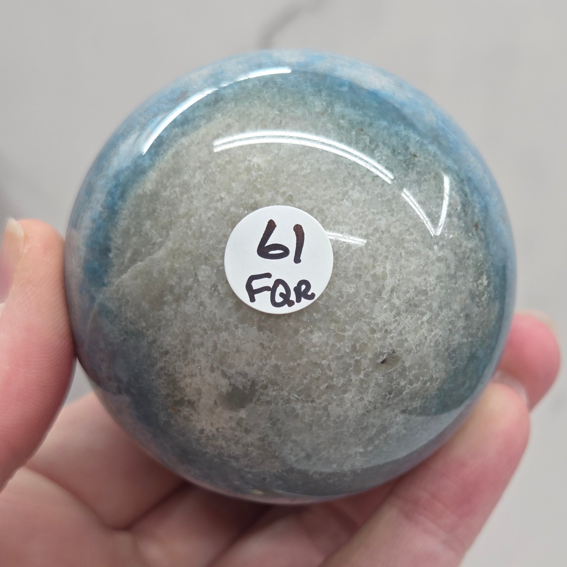 Trolleite sphere with blue and black colors being held in a hand against a white background
