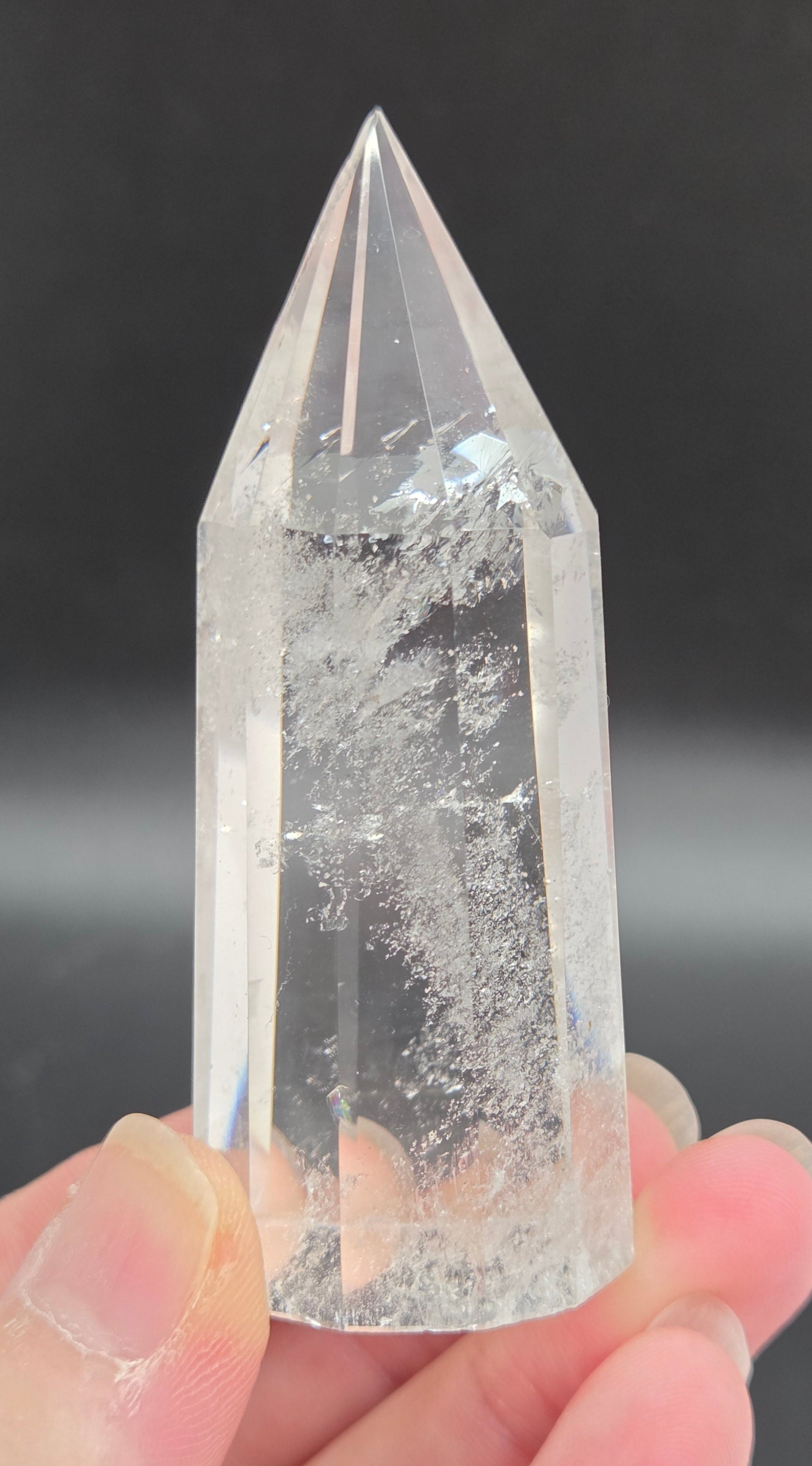 Clear crystal point held by a hand against a dark background