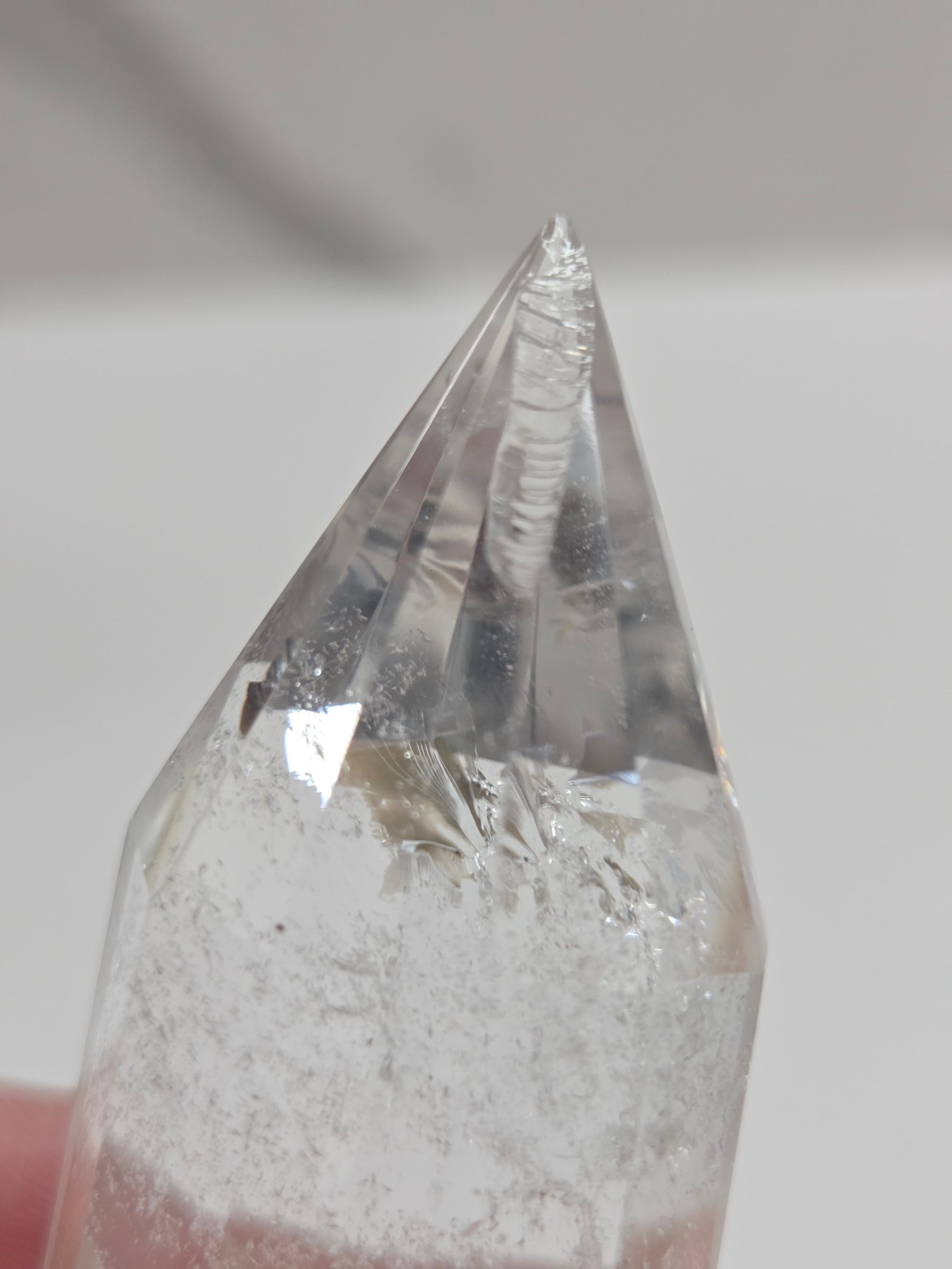 Crystal with a pointed tip held by a hand against a neutral background