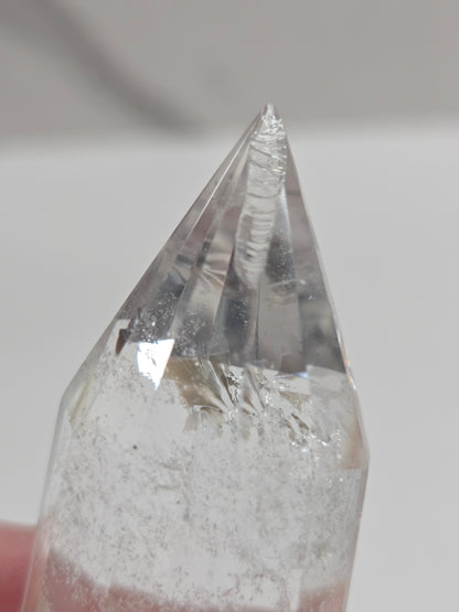 Crystal with a pointed tip held by a hand against a neutral background