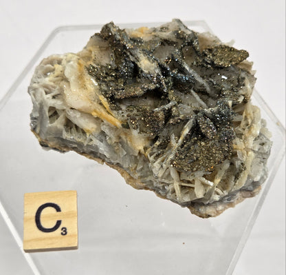 Mineral sample in a hexagonal clear container with a label on a white background