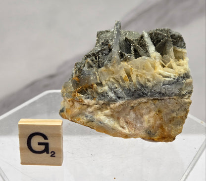 Mineral sample on a clear stand with a wooden block displaying 'G2' on a light gray background