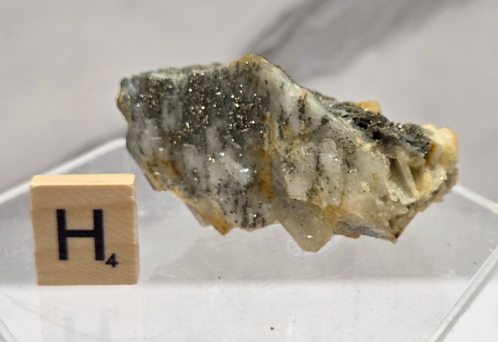 Mineral sample in a clear display case with a wooden label on a light gray background
