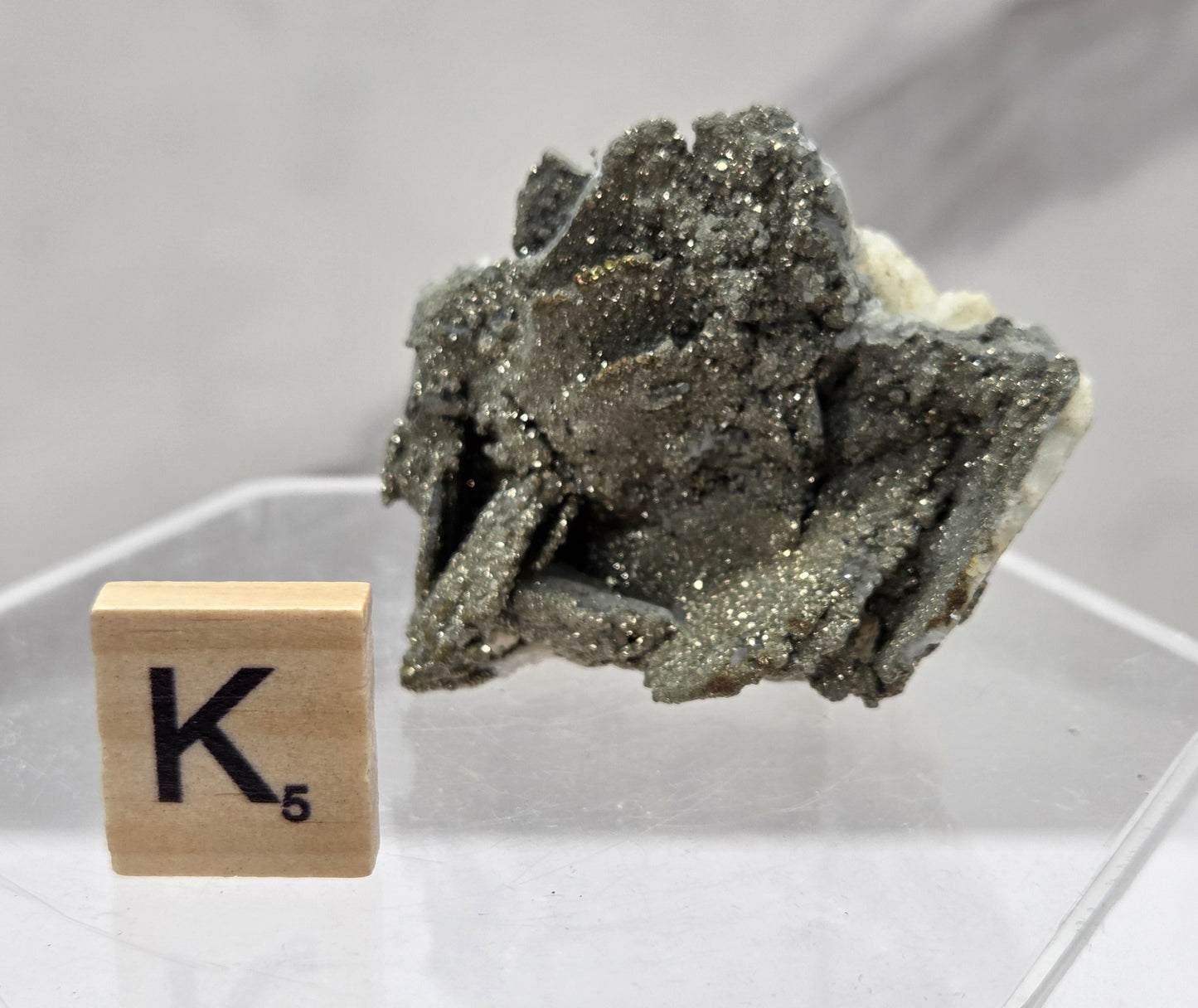 Mineral specimen on a stand with a wooden block displaying the letter 'K' on a white background