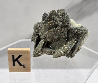Mineral specimen on a stand with a wooden block displaying the letter 'K' on a white background