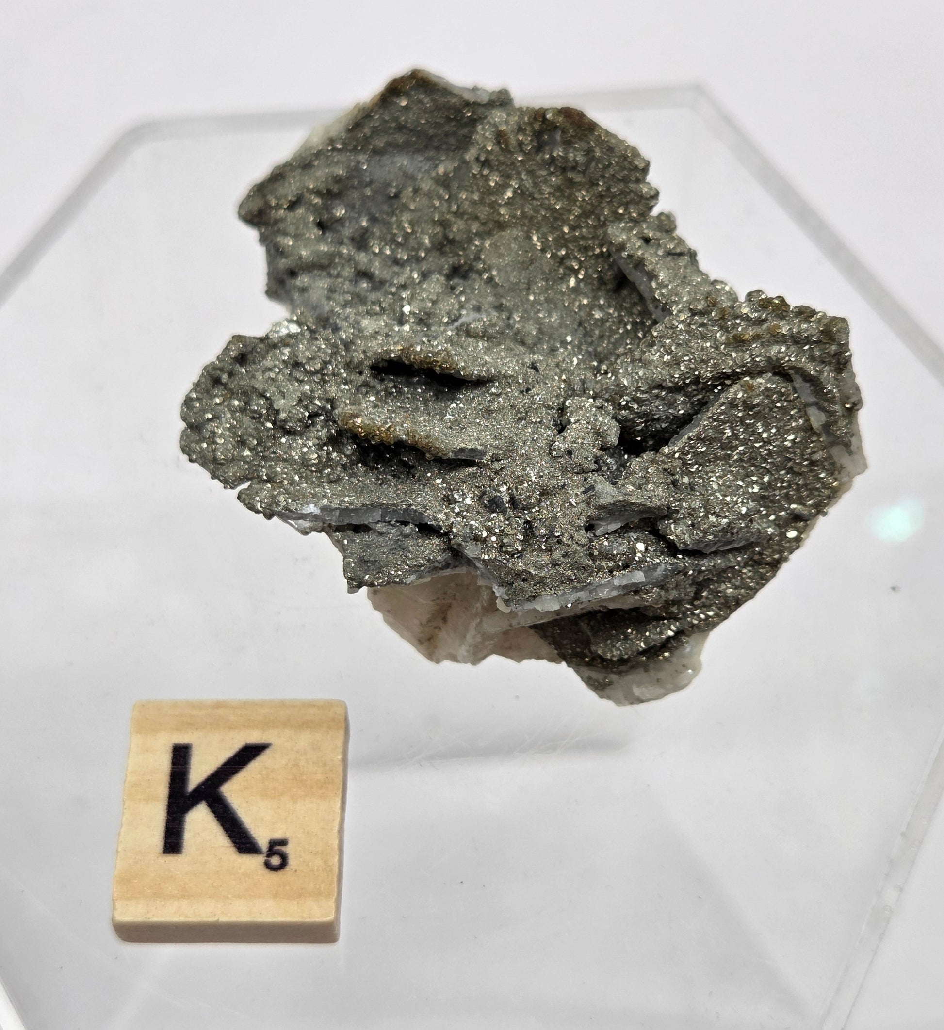 Mineral sample on a hexagonal stand with a wooden block labeled 'K5' on a white background