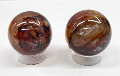Two polished spheres with a mix of golden healer and fire quartz on stands against a white background