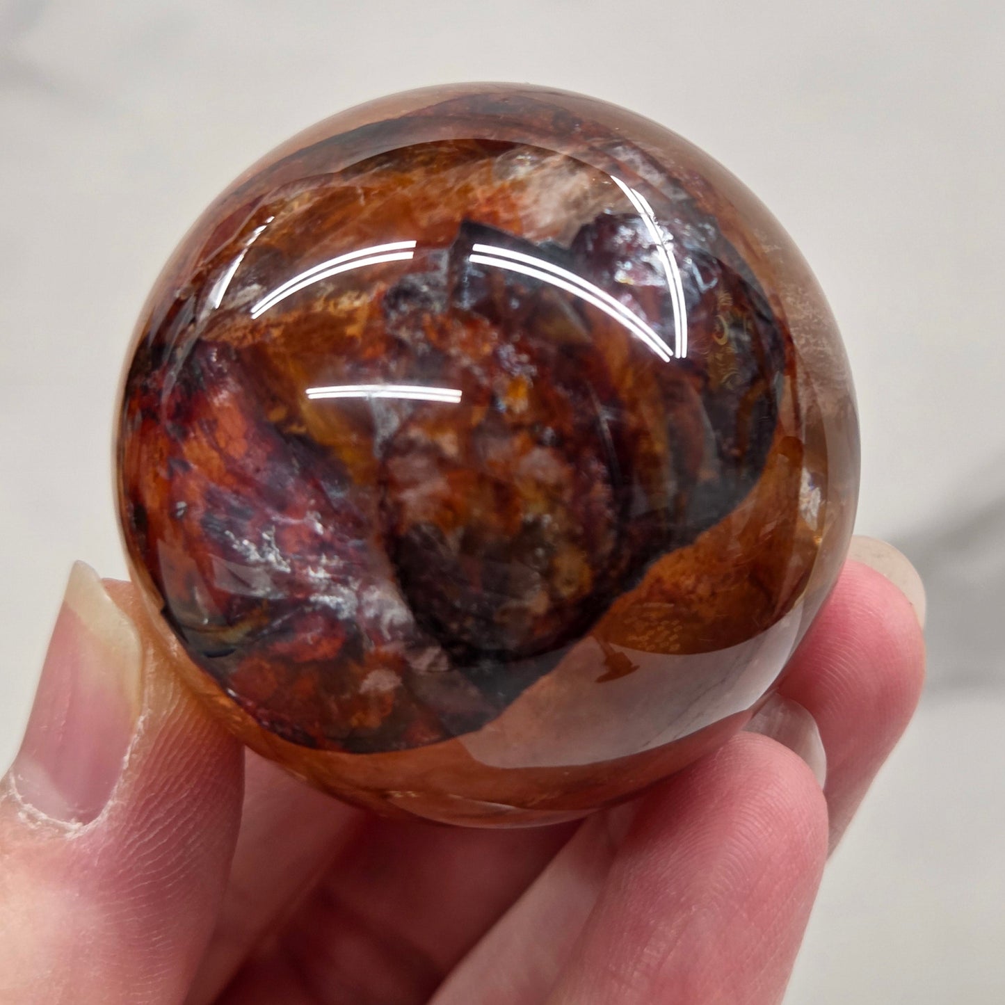 Hand holding a polished sphere with a mix of golden healer and fire quartz  against a white background