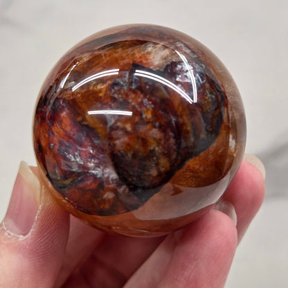 Hand holding a polished sphere with a mix of golden healer and fire quartz  against a white background