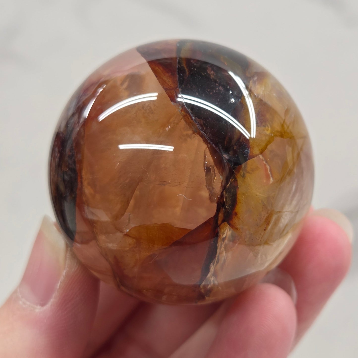 Hand holding a polished sphere with a mix of golden healer and fire quartz  against a white background