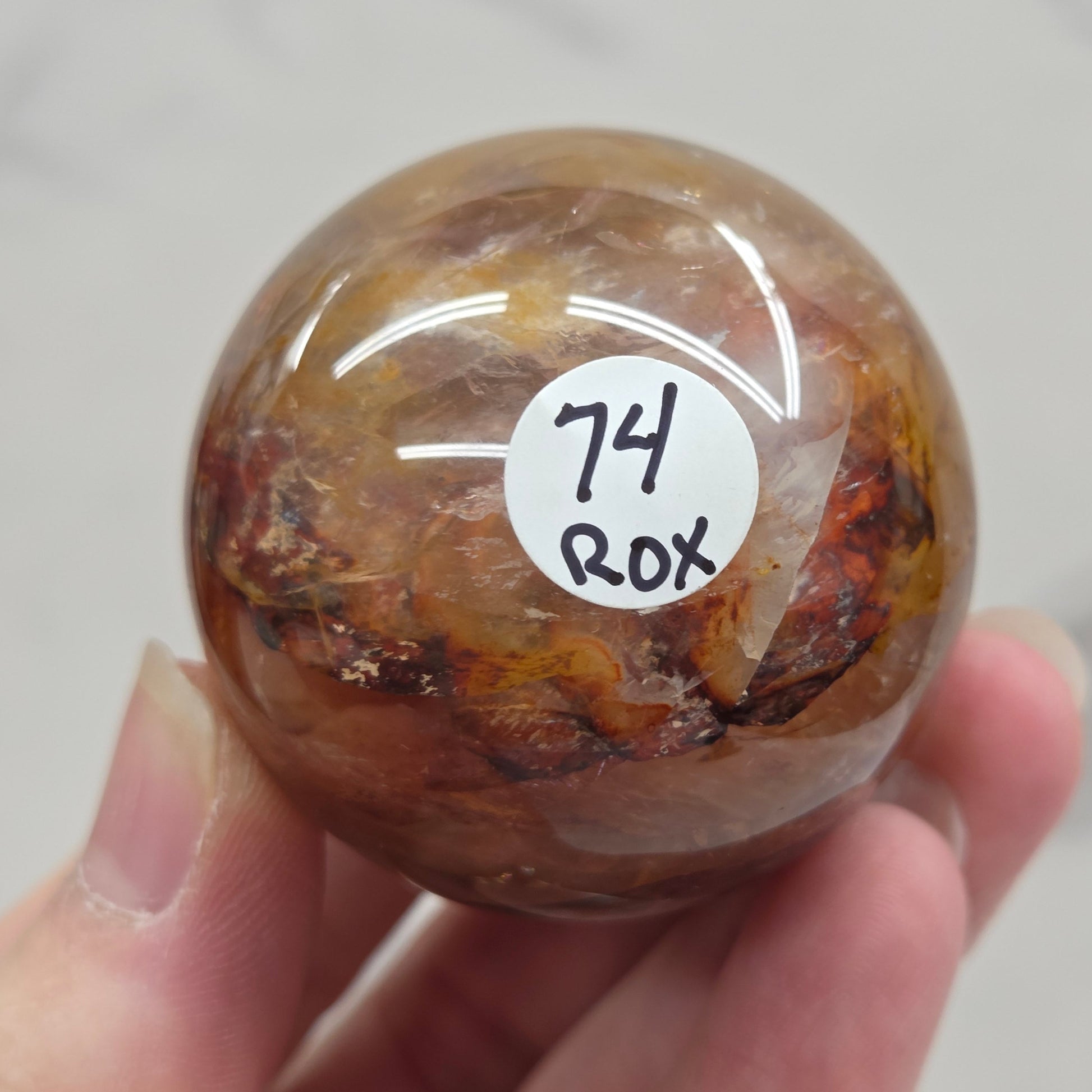 Hand holding a polished sphere with a mix of golden healer and fire quartz  against a white background