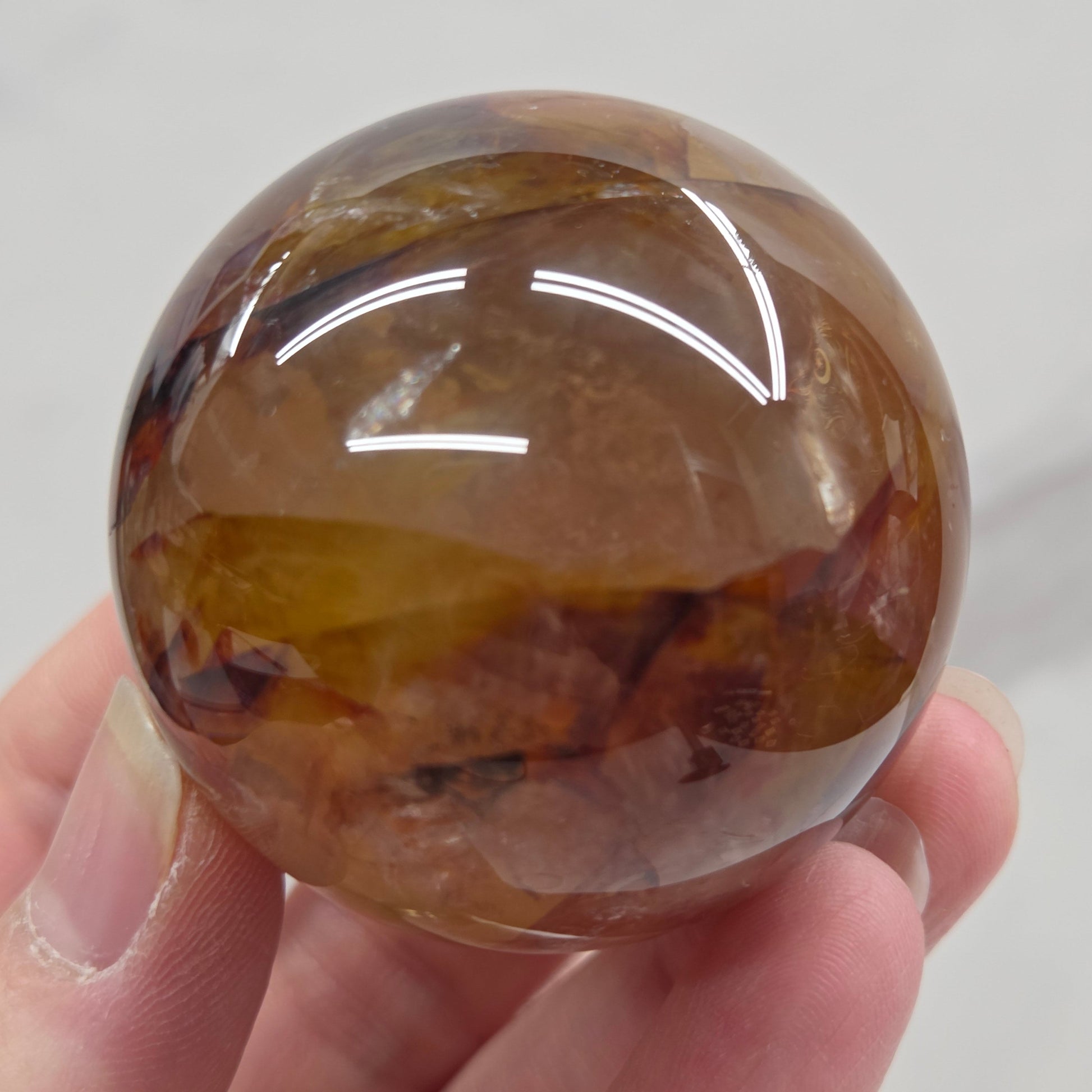 Hand holding a polished sphere with a mix of golden healer and fire quartz  against a white background