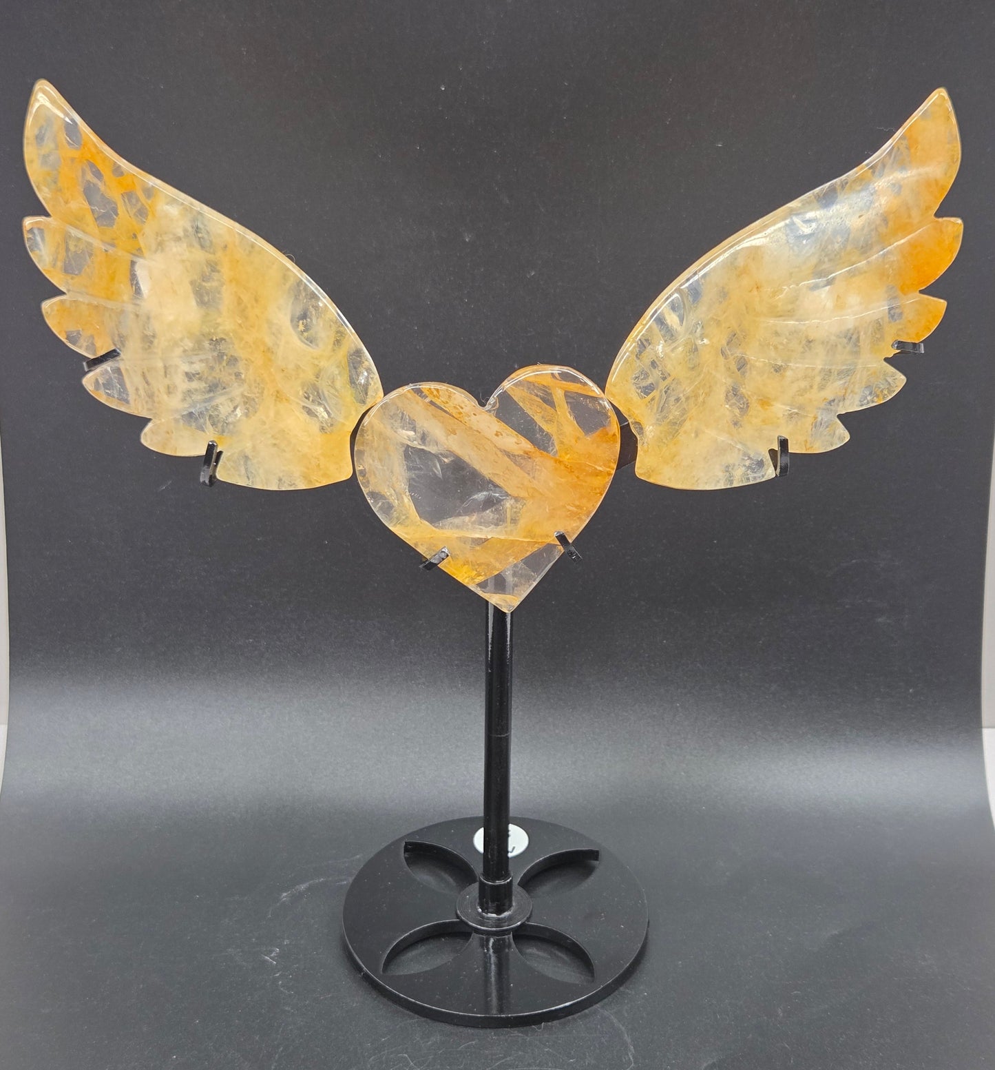 Decorative golden healer wings with a heart on a black stand against a gray background