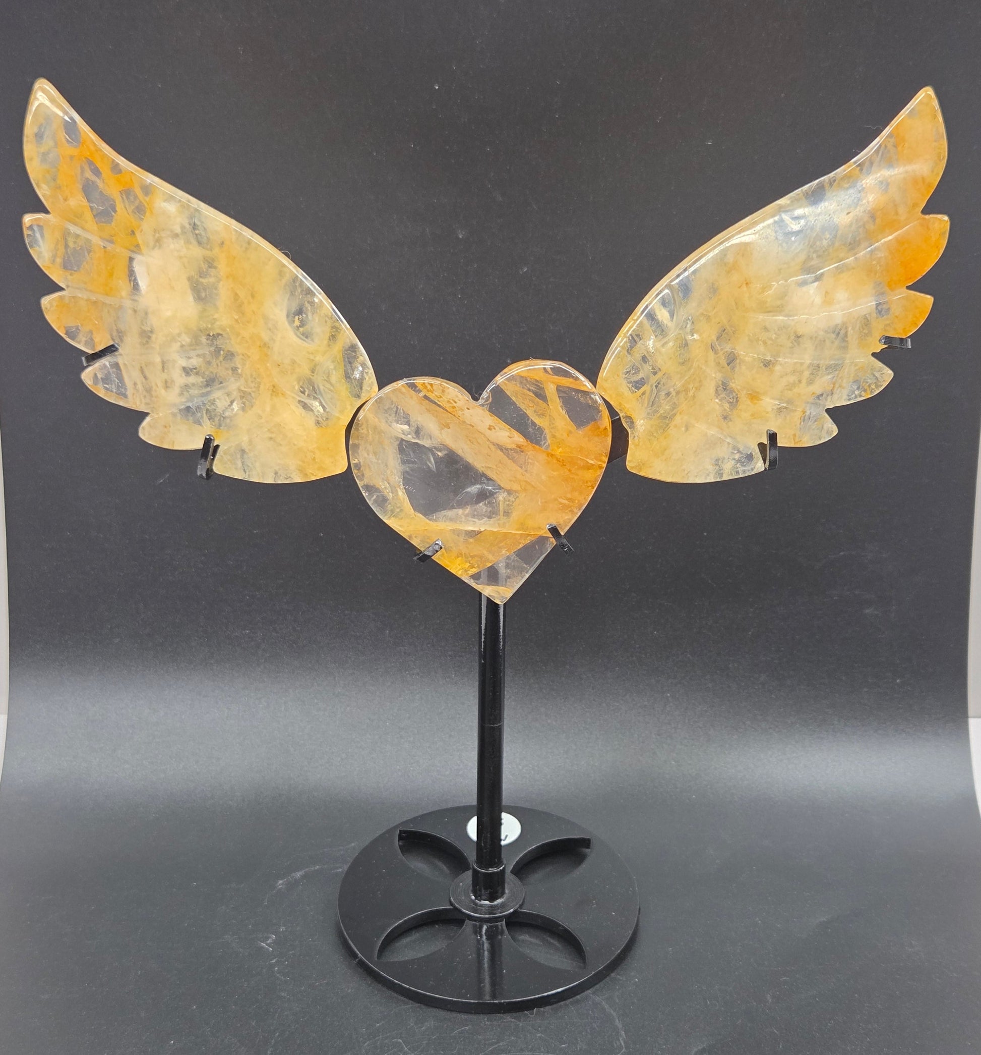 Decorative golden healer wings with a heart on a black stand against a gray background