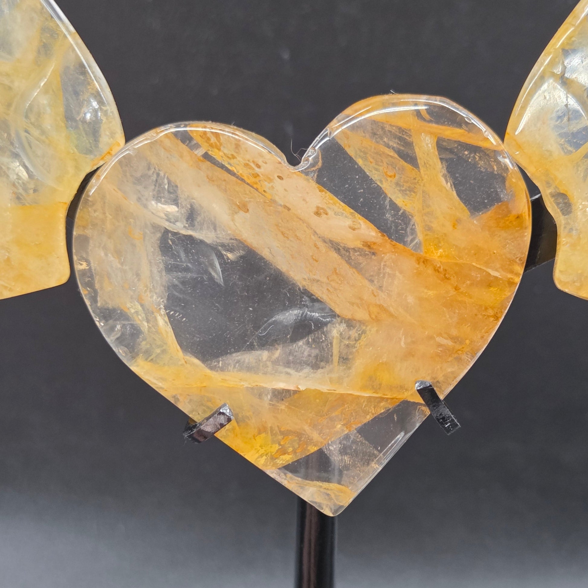 Decorative golden healer wings with a heart on a black stand against a gray background