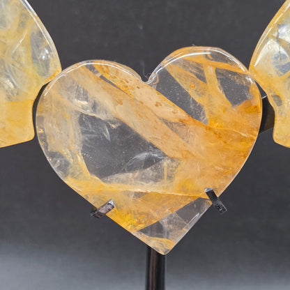 Decorative golden healer wings with a heart on a black stand against a gray background