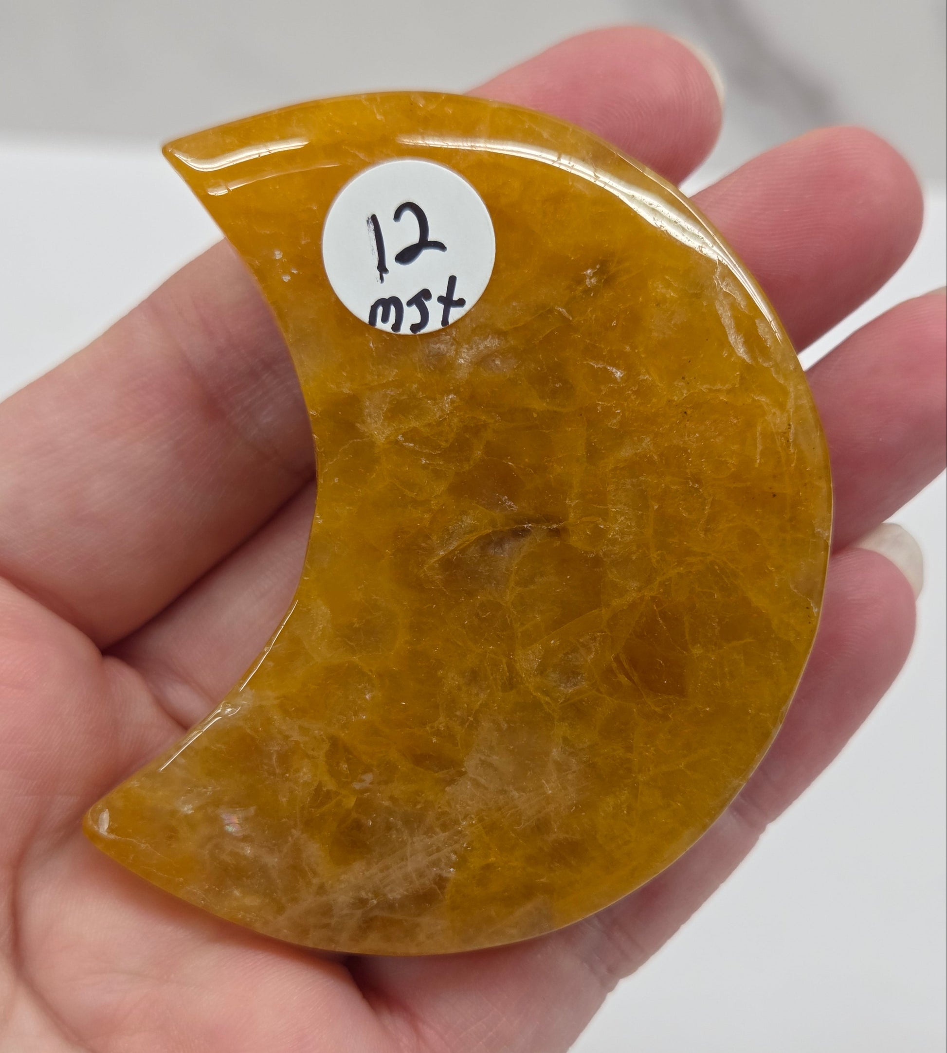 Hand holding a golden healer semi-circular stone against a white background