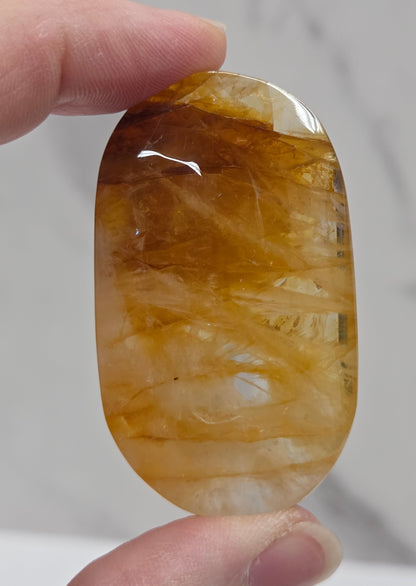 Hand holding a polished golden healer stone on a white background
