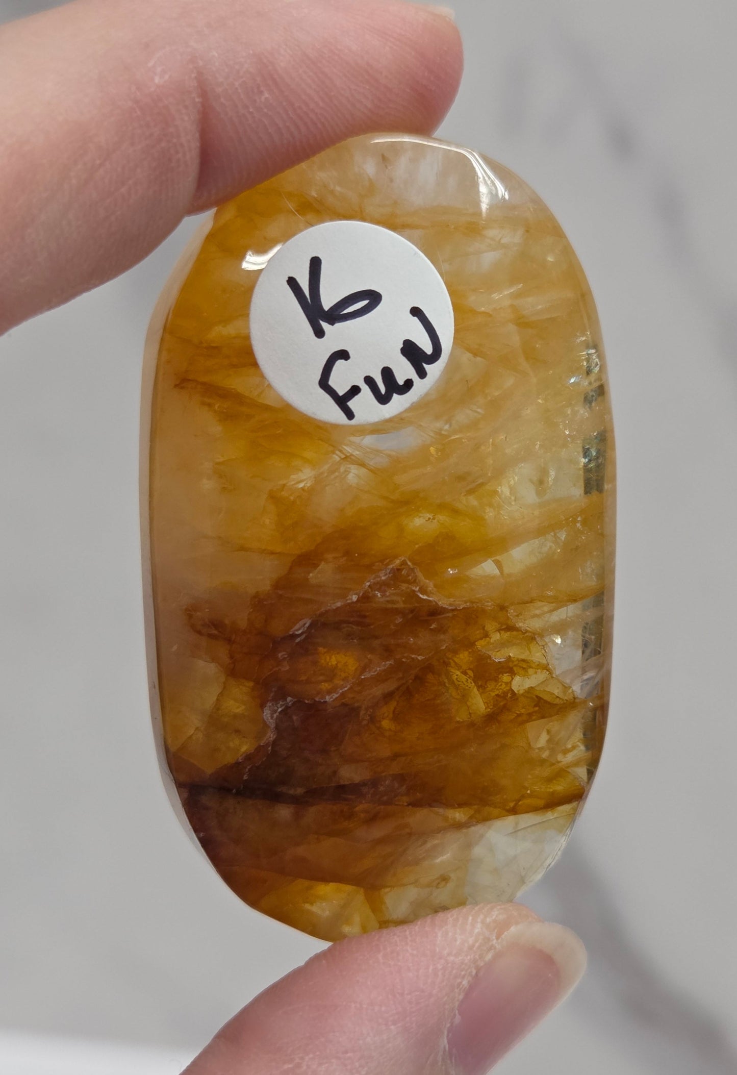 Hand holding a polished golden healer stone on a white background