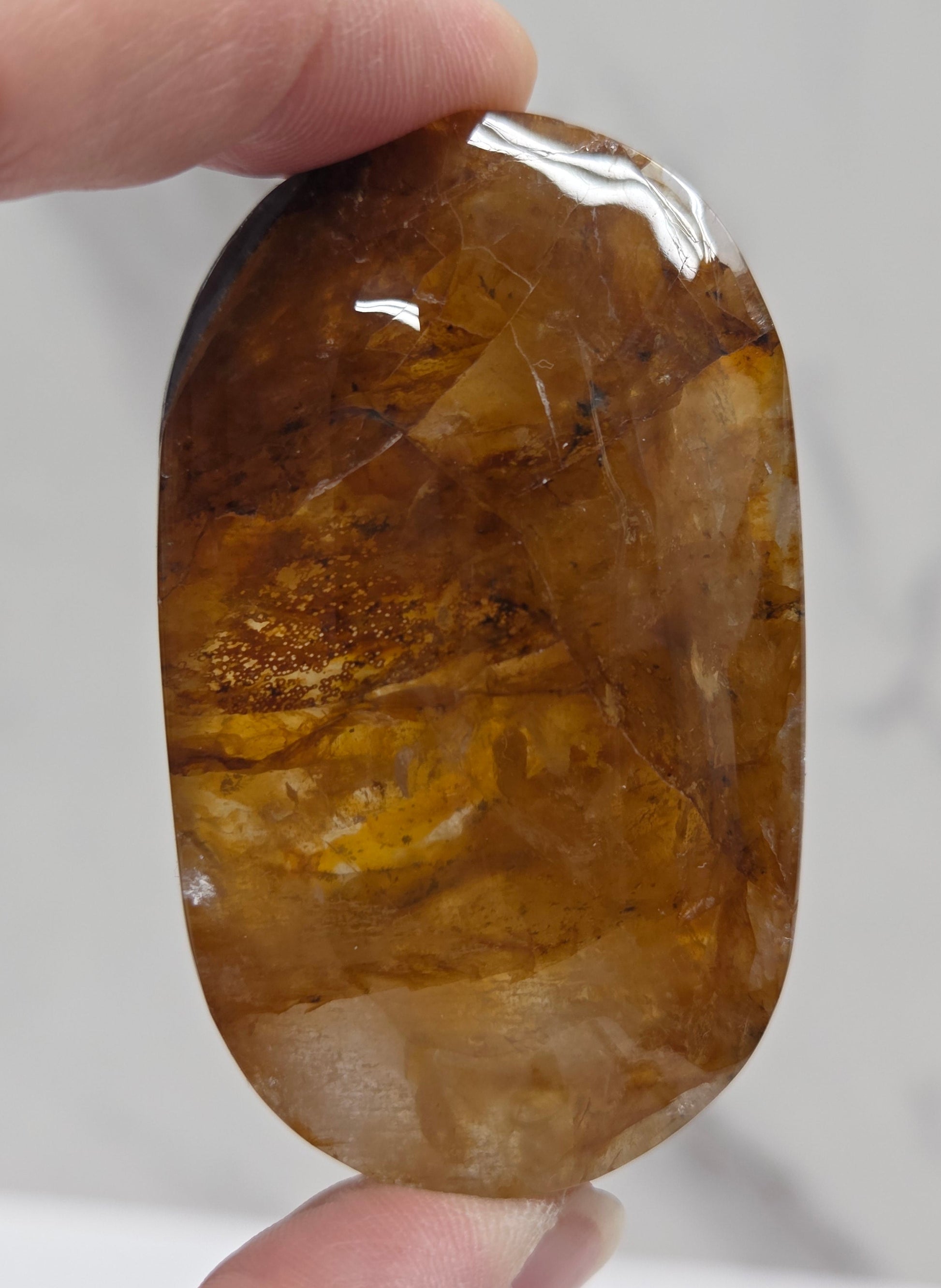 Hand holding a polished golden healer stone on a white background