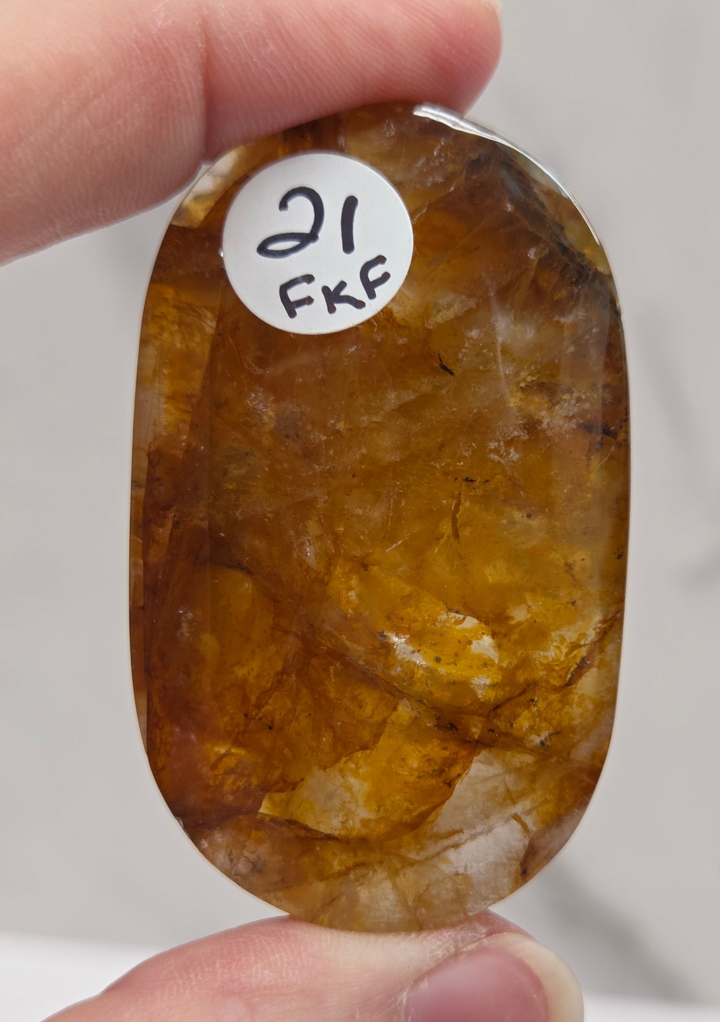 Hand holding a polished golden healer stone on a white background