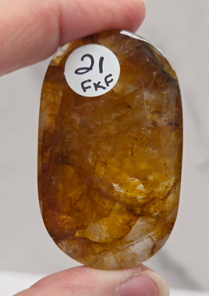 Hand holding a polished golden healer stone on a white background