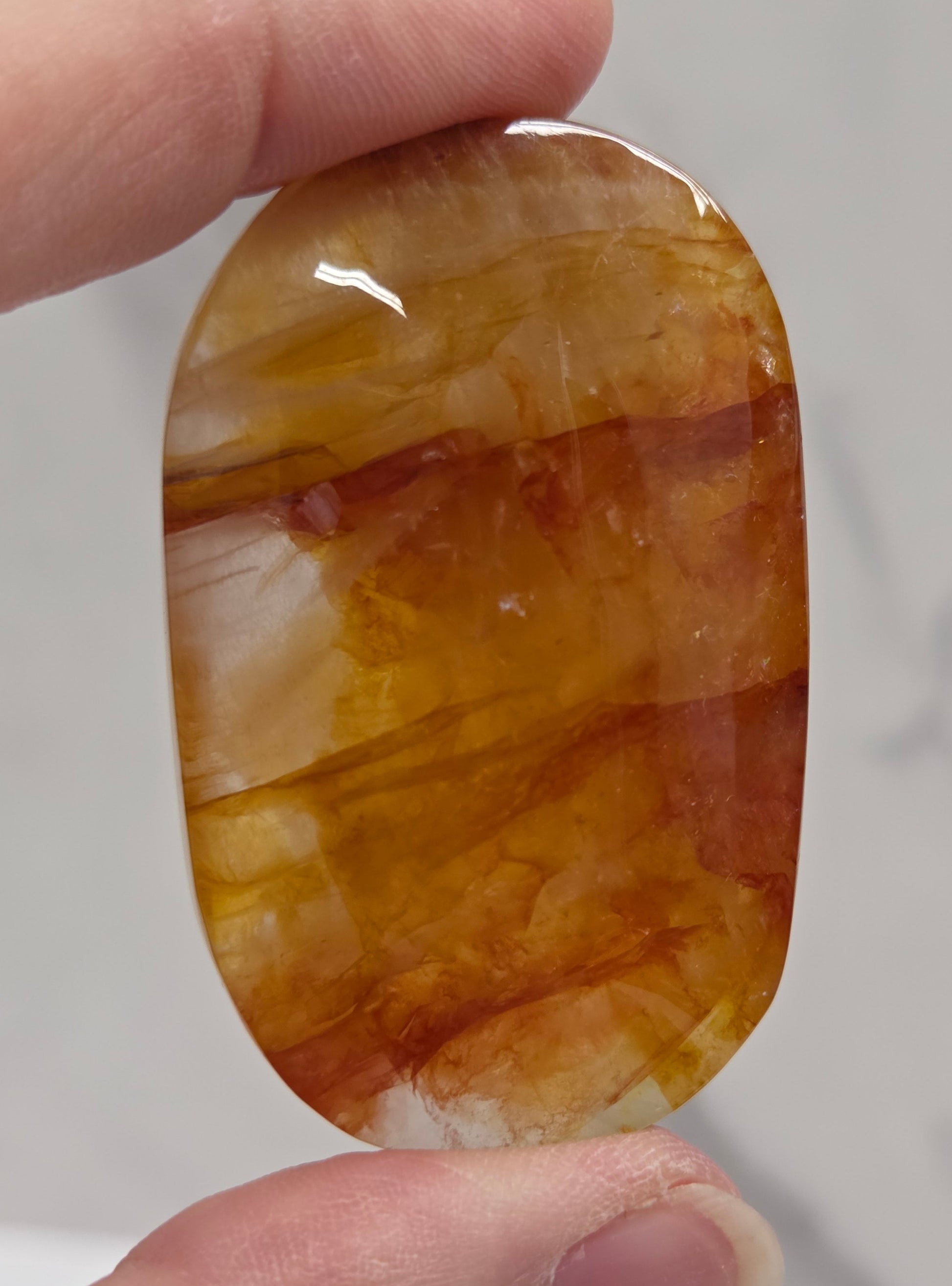 Hand holding a polished golden healer stone on a white background