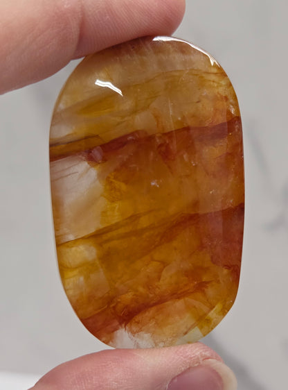Hand holding a polished golden healer stone on a white background