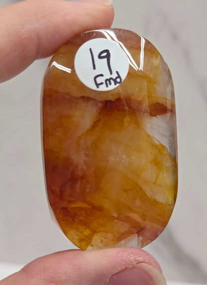 Hand holding a polished golden healer stone on a white background
