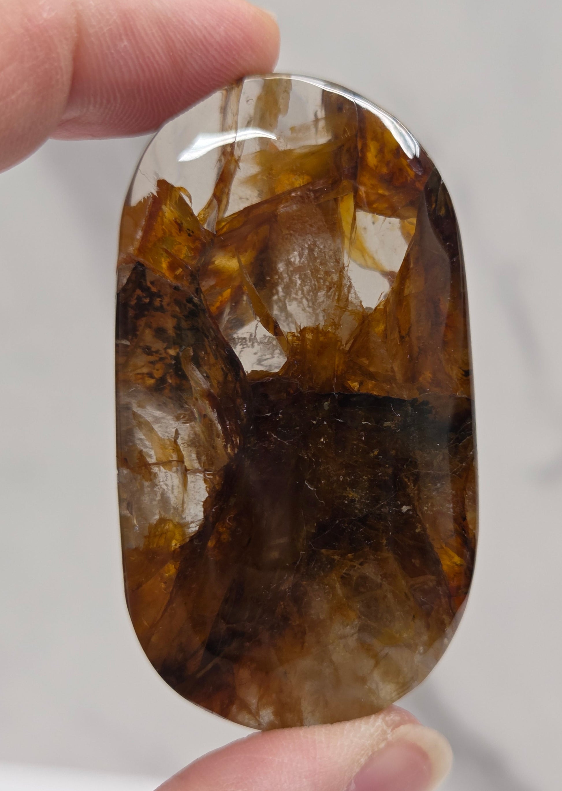 Hand holding a polished golden healer stone on a white background