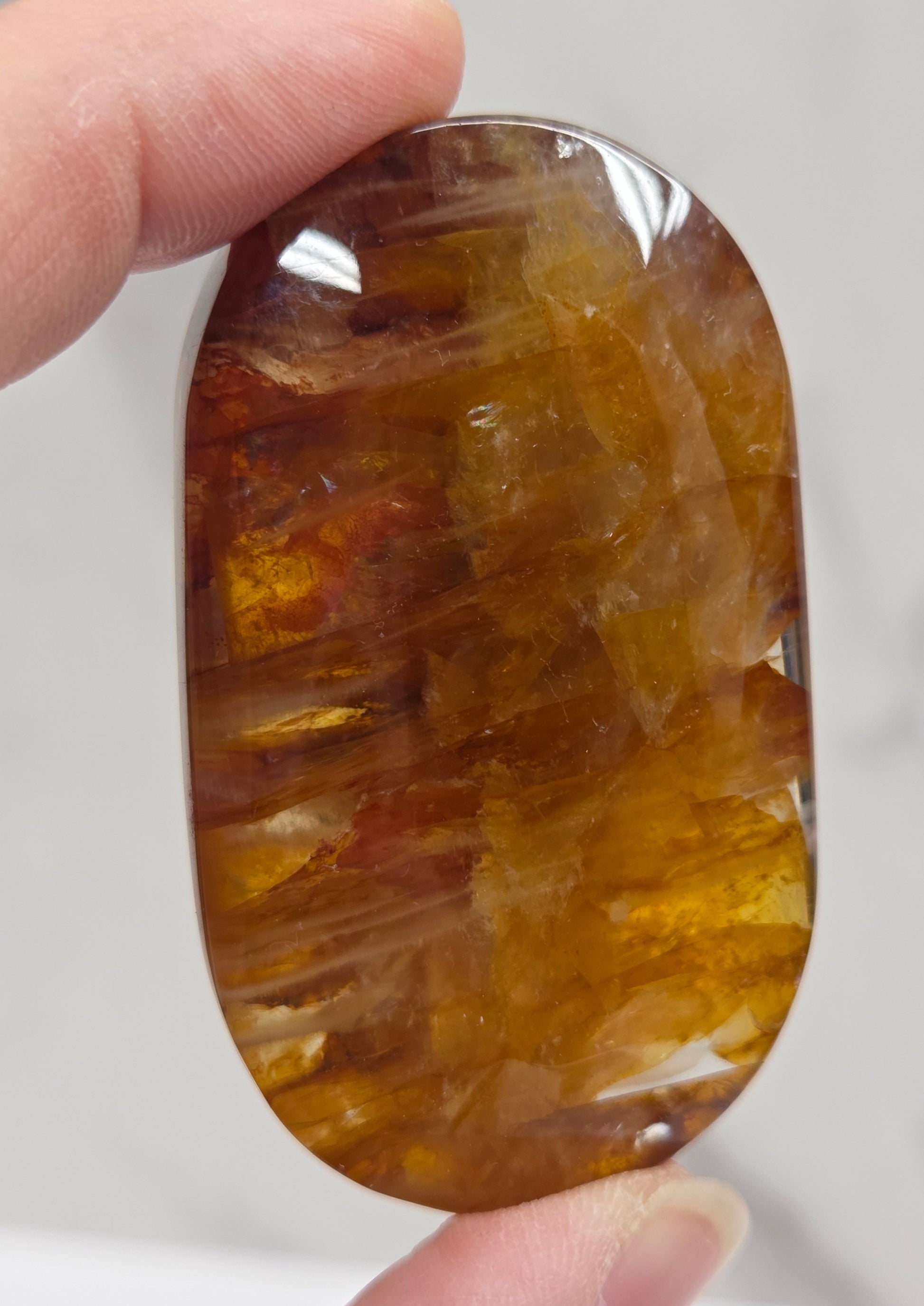 Hand holding a polished golden healer stone on a white background