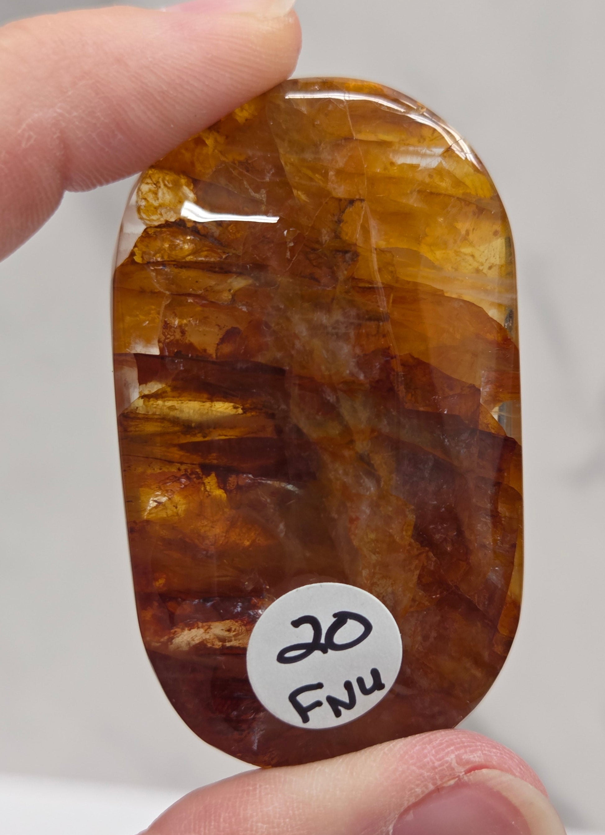 Hand holding a polished golden healer stone on a white background