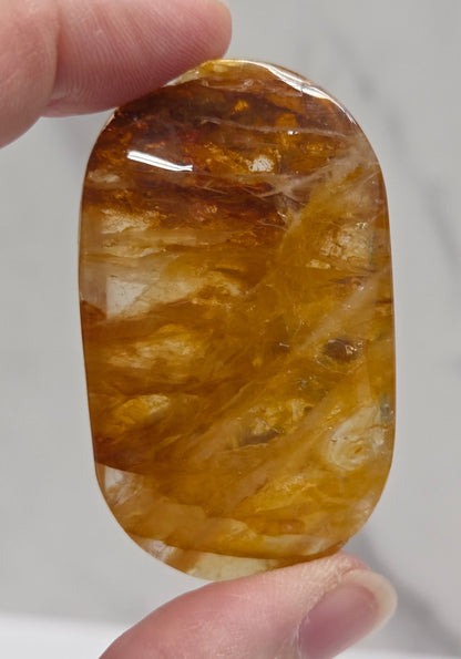 Hand holding a polished golden healer stone on a white background