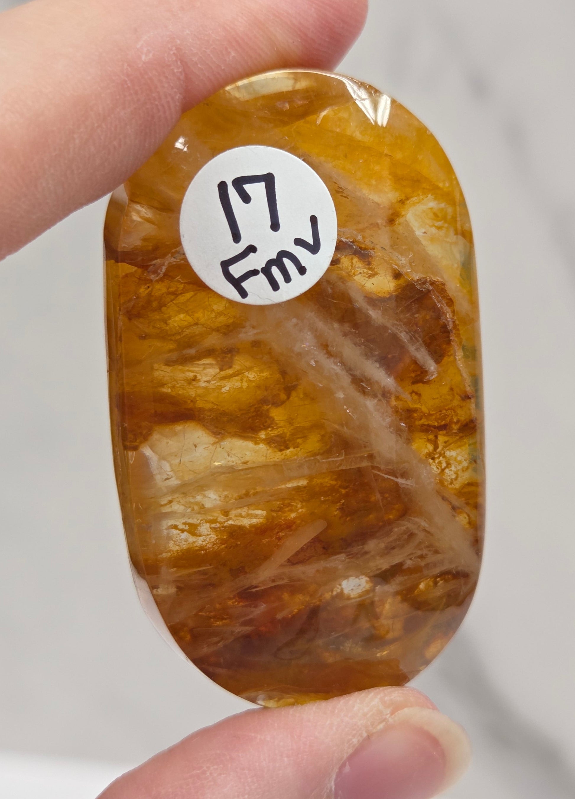 Hand holding a polished golden healer stone on a white background