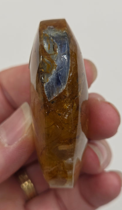 Hand holding a polished golden healer stone on a white background
