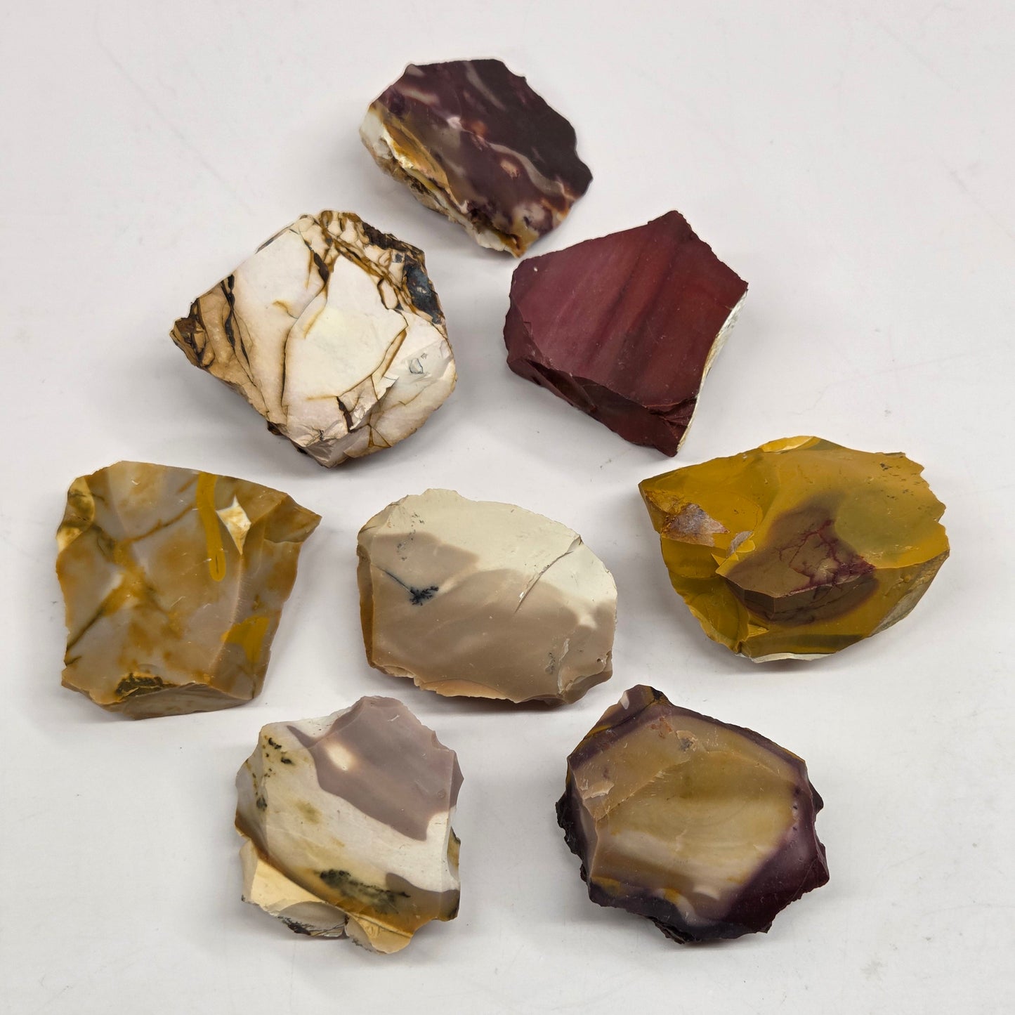 Collection of various raw mookaite stone specimens on a light gray background