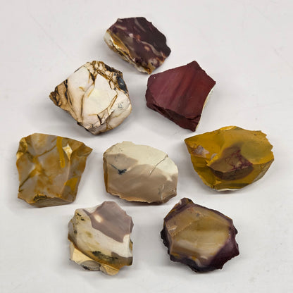 Collection of various raw mookaite stone specimens on a light gray background