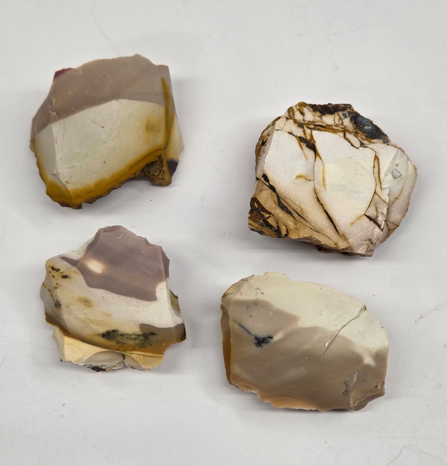 Collection of various raw mookaite stone specimens on a light gray background