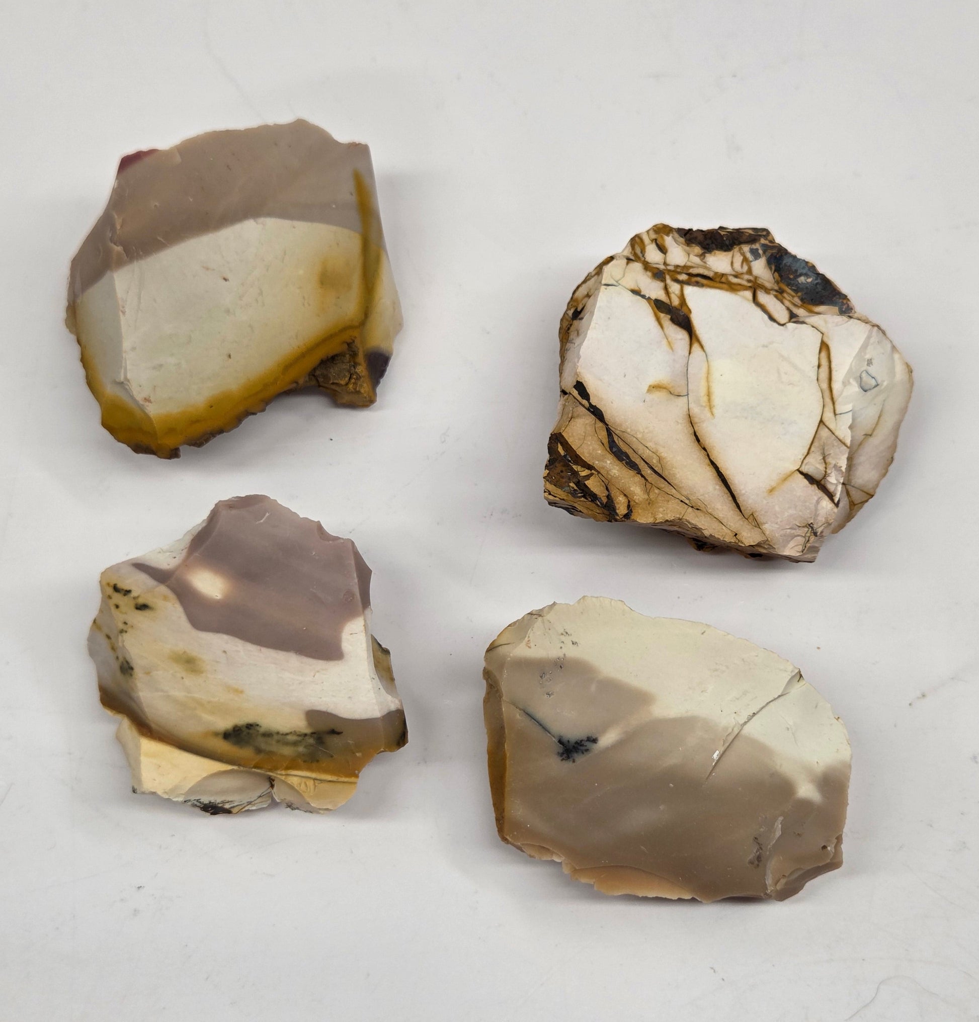 Collection of various raw mookaite stone specimens on a light gray background