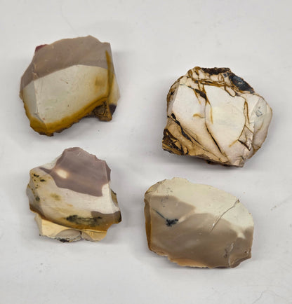 Collection of various raw mookaite stone specimens on a light gray background