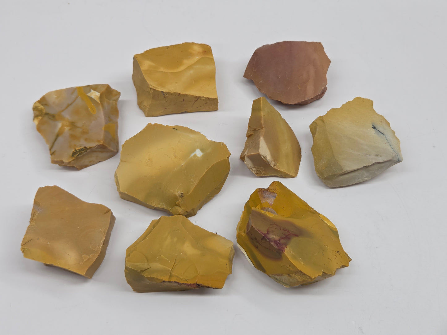 Collection of various raw mookaite stone specimens on a light gray background