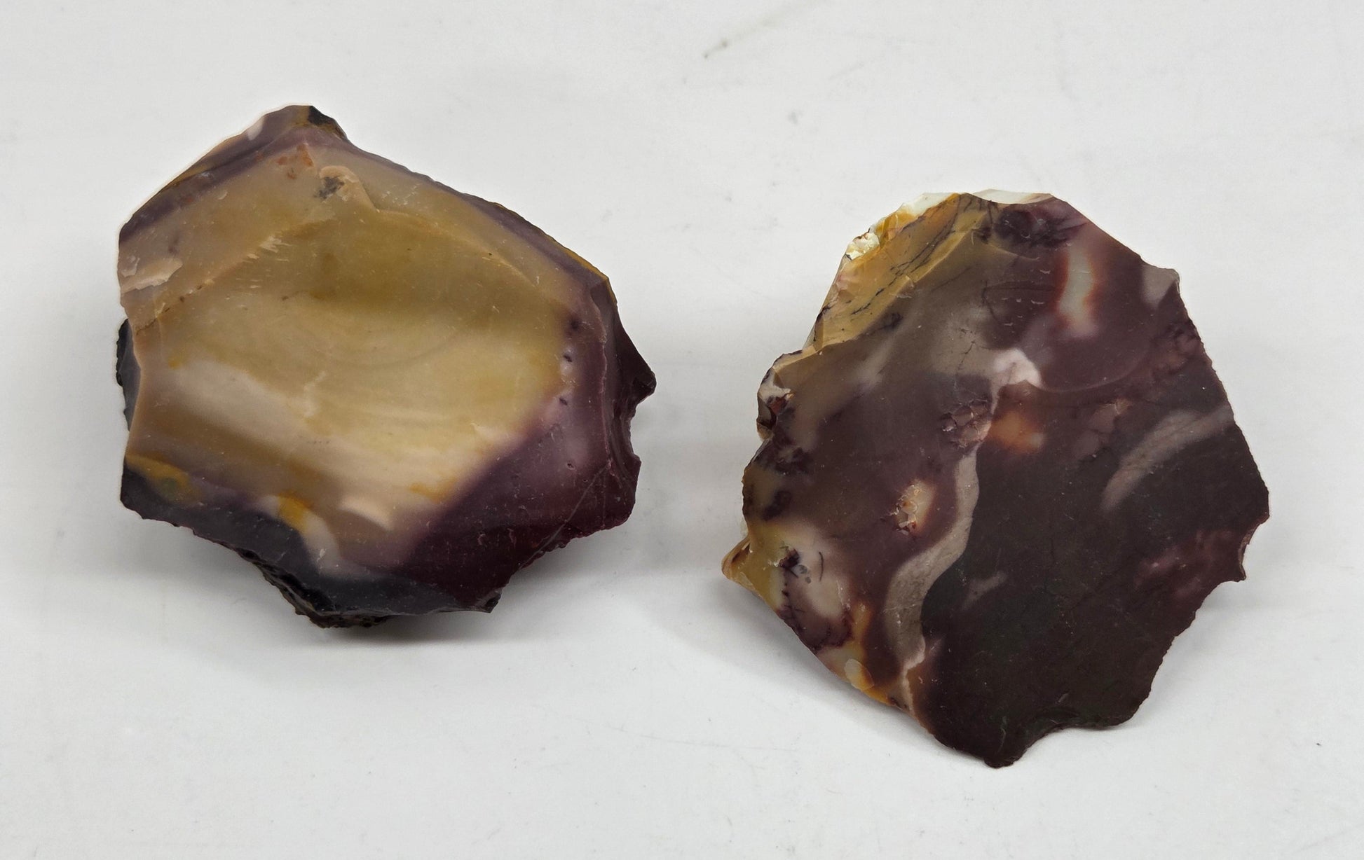 Collection of various raw mookaite stone specimens on a light gray background