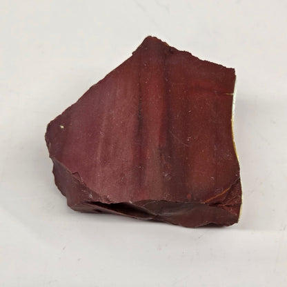 A raw mookaite stone specimen on a light gray background