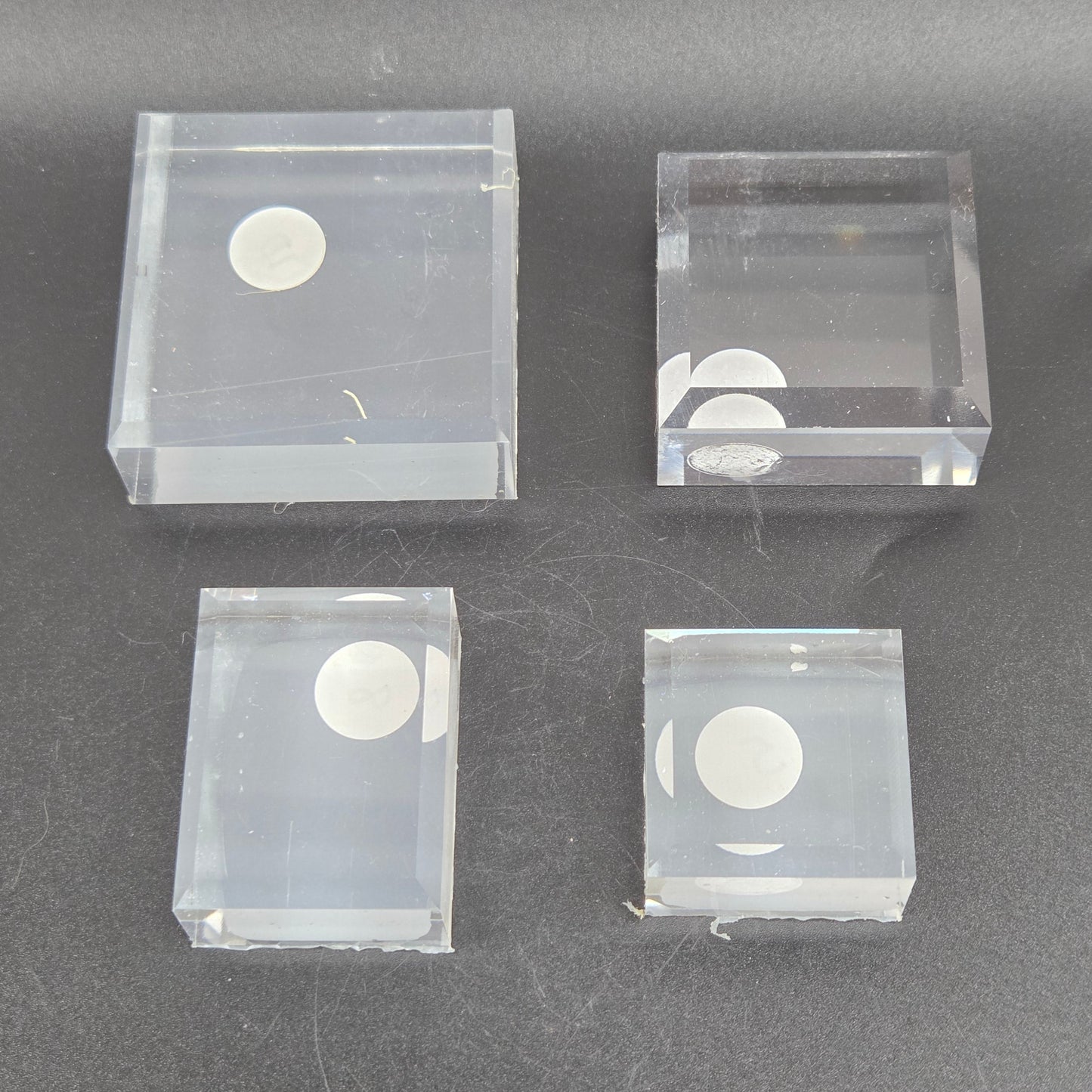 Four clear plastic blocks with circular cutouts on a dark gray background