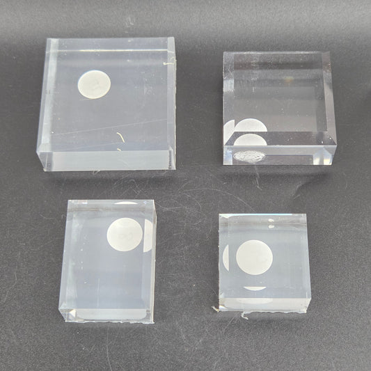Four clear plastic blocks with circular cutouts on a dark gray background
