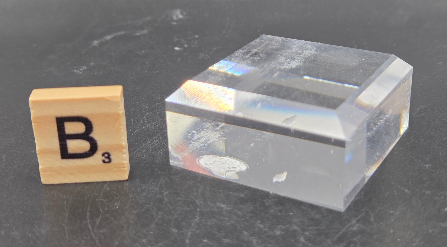 Clear plastic block and wooden letter 'B' on a dark surface