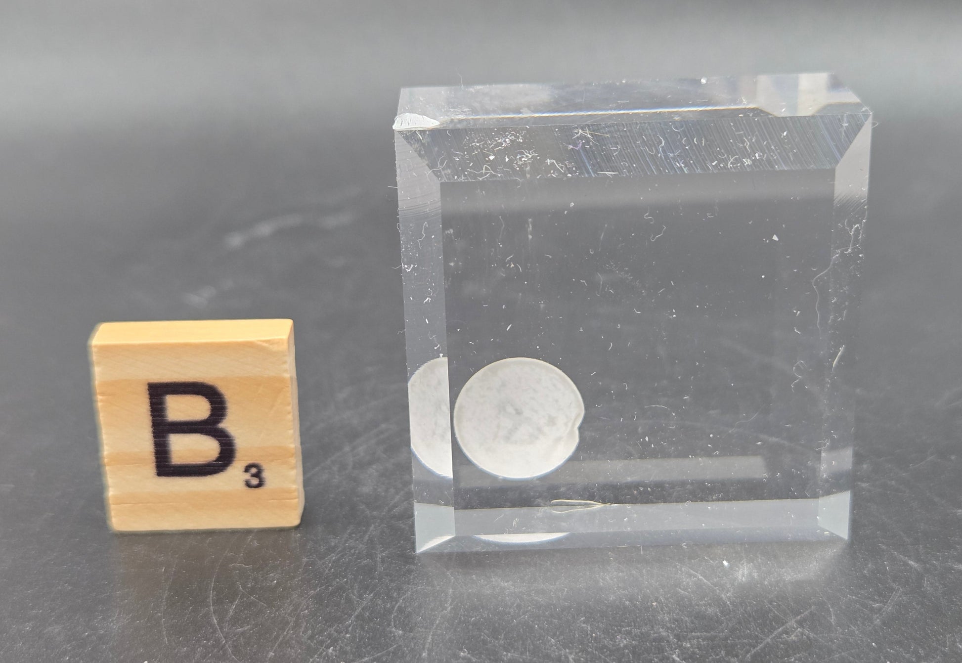 Clear rectangular block with a coin inside, next to a wooden block with 'B' and '3' on a gray background