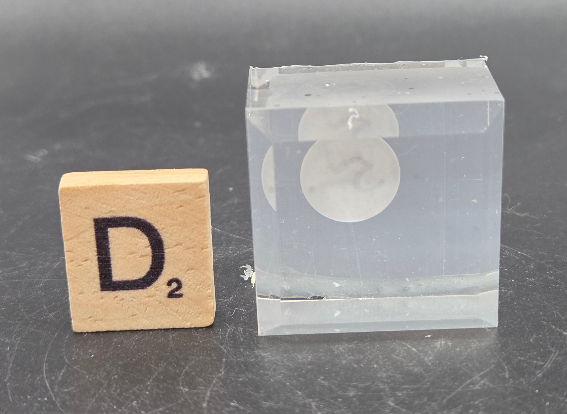 Small wooden block with 'D2' and a clear plastic block on a gray surface