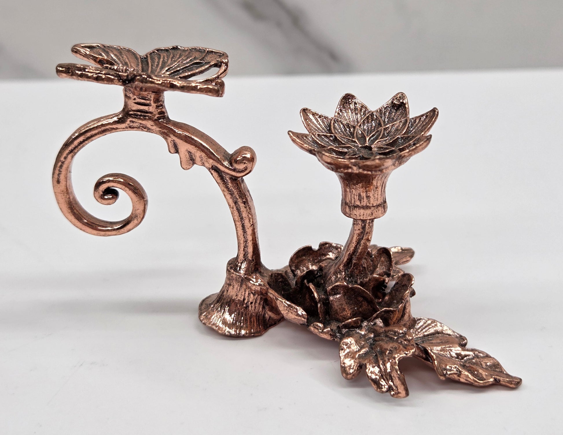 Decorative sphere stand, in rose gold with a butterfly and flower shape, on a white surface with a gray background.