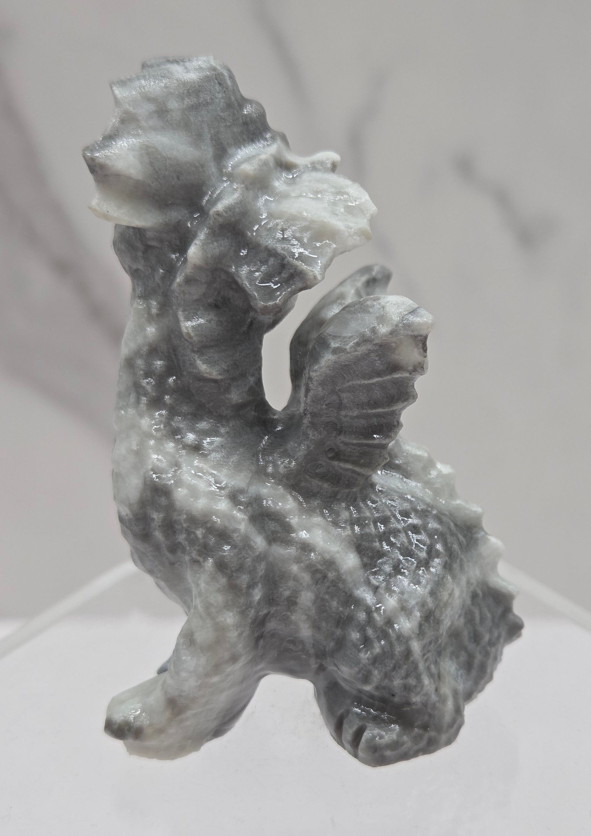 Grey & white crystal dragon carving on an acrylic stand against a neutral background